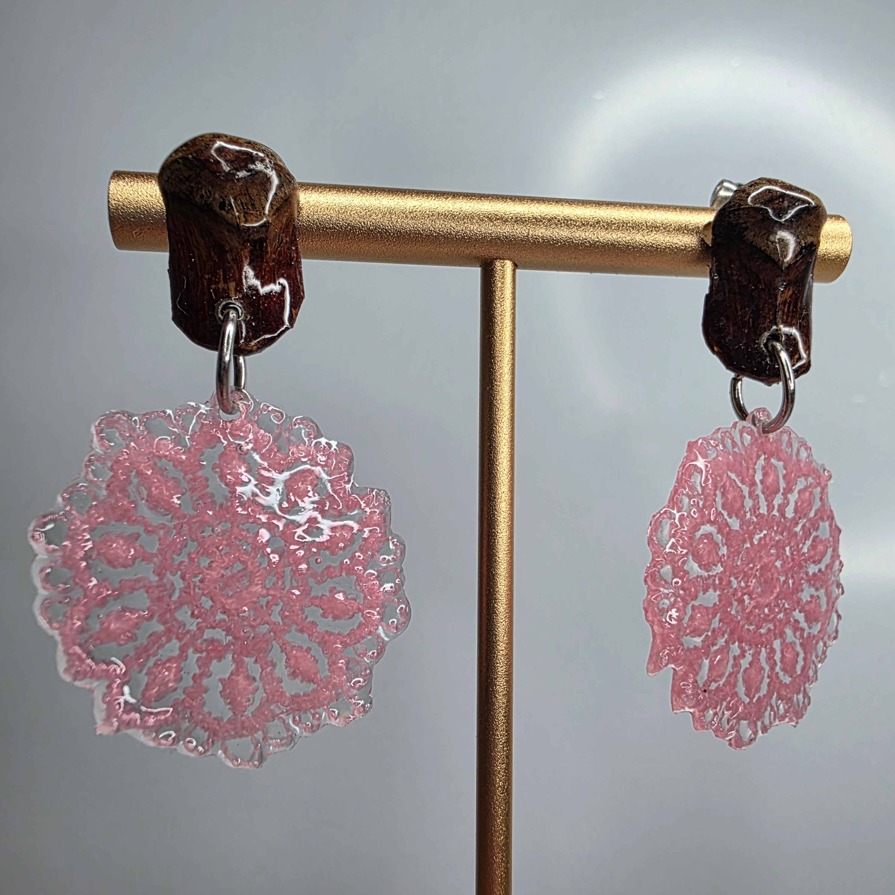 Pendientes de encaje redondo with pink intricate resin lace design and dark wooden hooks on gold stand
