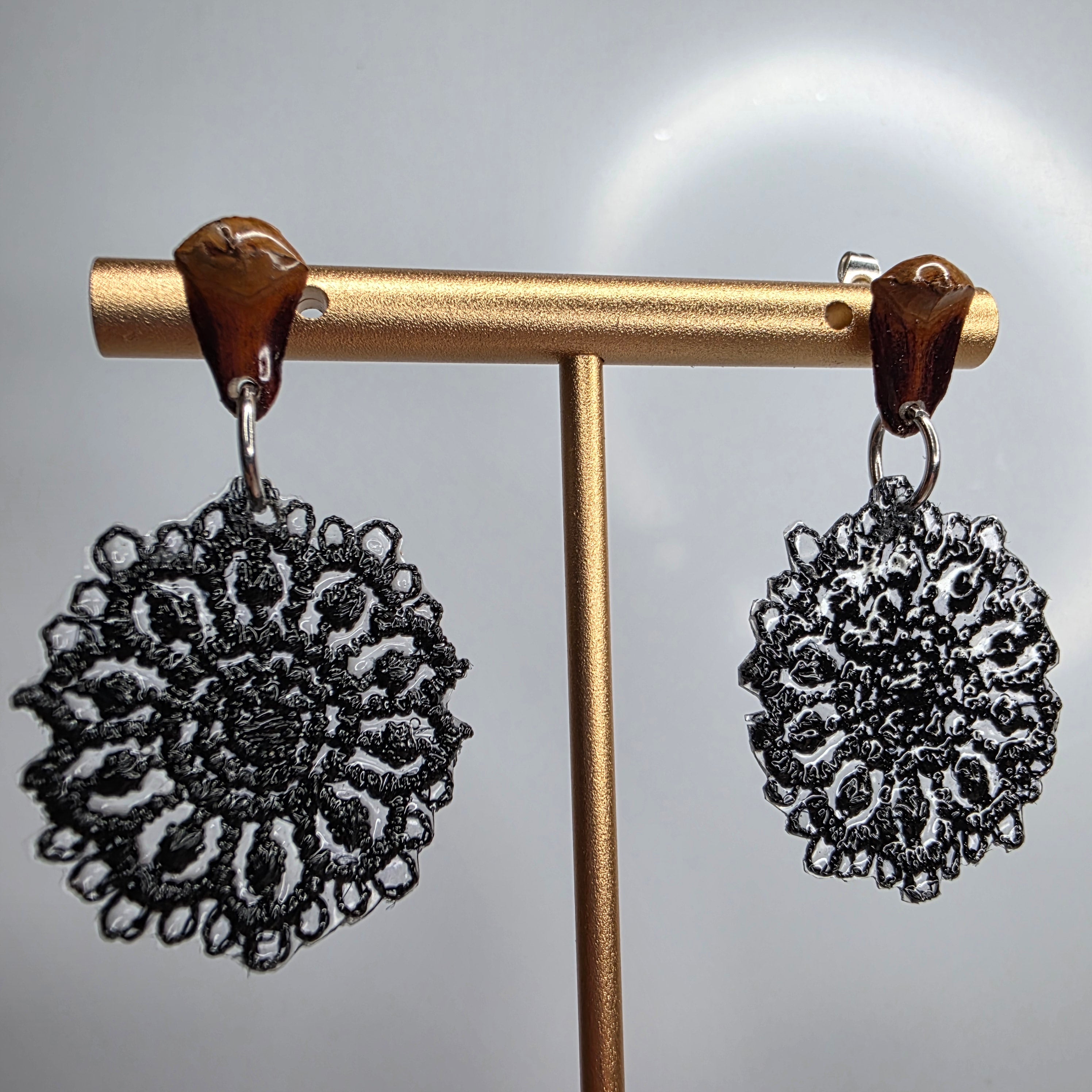 Black lace round earrings with brown resin studs displayed on a gold stand, Pendientes de encaje redondo