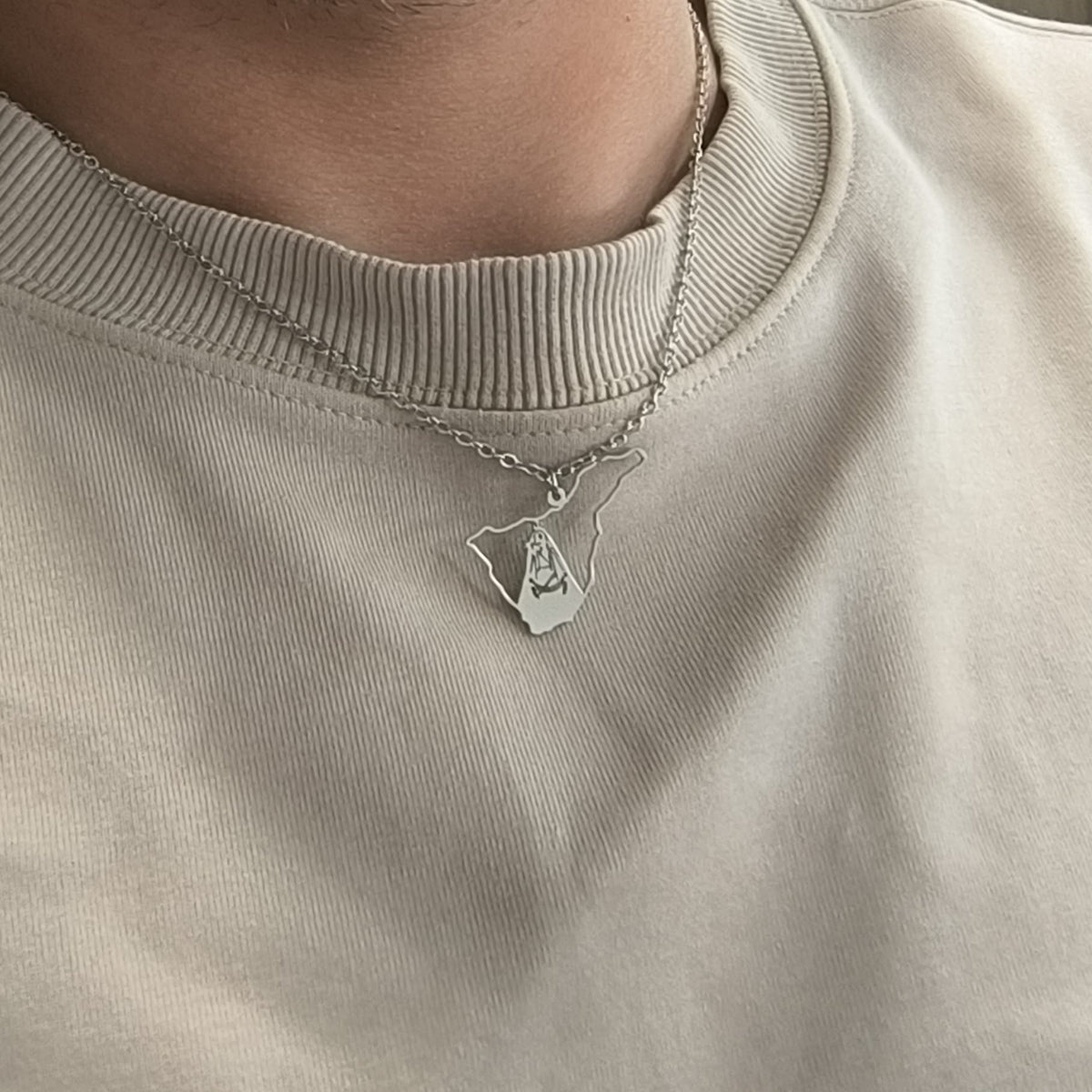 Collar de la Virgen de Candelaria de Tenerife en acabado plateado, llevado sobre una camiseta